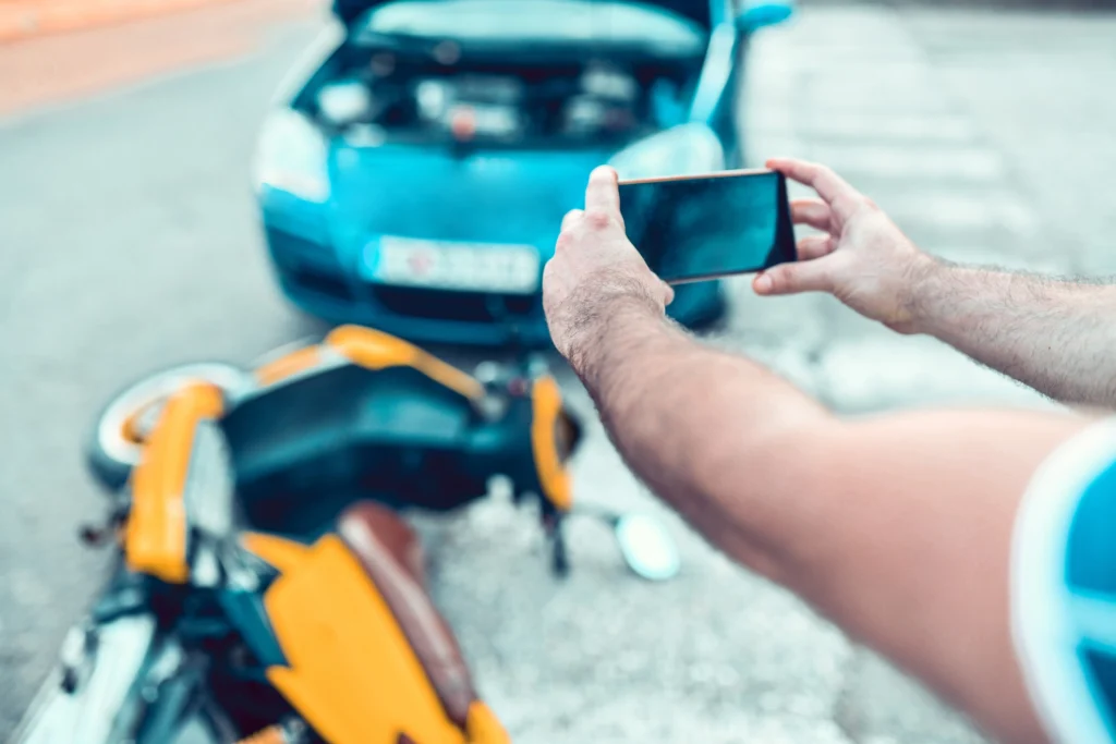 Man using his phone to photograph damage after a motorcycle accident